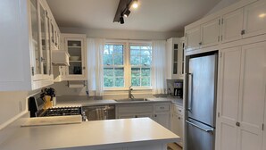 A modern kitchen with white cabinets, a stainless steel refrigerator, a built-in oven, and a large window. - 4-bedroom house in charming Wainscott walking distance to the beach (East Hampton)