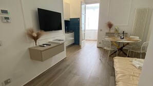 Habitació moderna i ben il·luminada amb televisió de pantalla plana, taula de dinar amb cadires, llit i zona de cuina amb rajoles blaves.