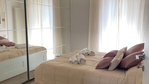 Un dormitori amb un llit, una taula de nit, un mirall i una finestra amb cortines.
