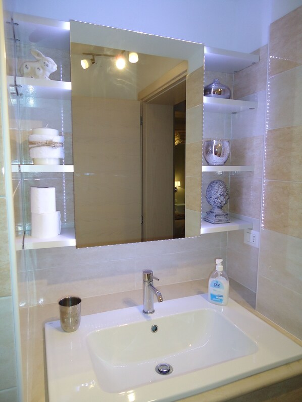 Une salle de bain avec un lavabo blanc, un miroir et des étagères contenant des articles de toilette.