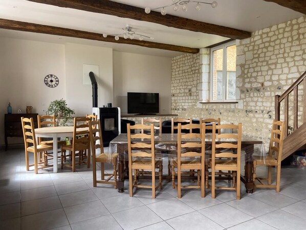 A dining area with a round table and wooden chairs, a television, and a stone wall.