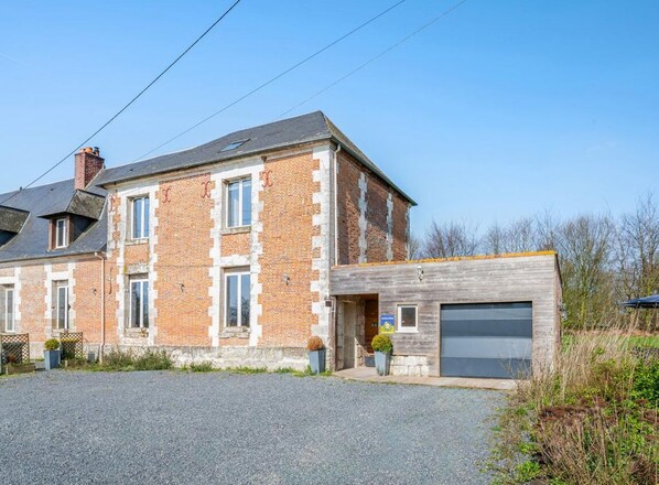 A two-story brick house with a garage, a gravel driveway, and a small garden area.
