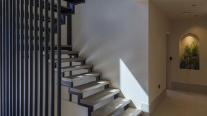 Eine moderne Treppe mit geometrischem Design, die zu einem Flur mit Pflanze und einer eingelassenen Deckenleuchte führt.