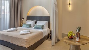Ein modernes Hotelzimmer mit einem großen Bett, einem runden Holztisch mit Obst und einer Flasche sowie einer Wandleuchte.
