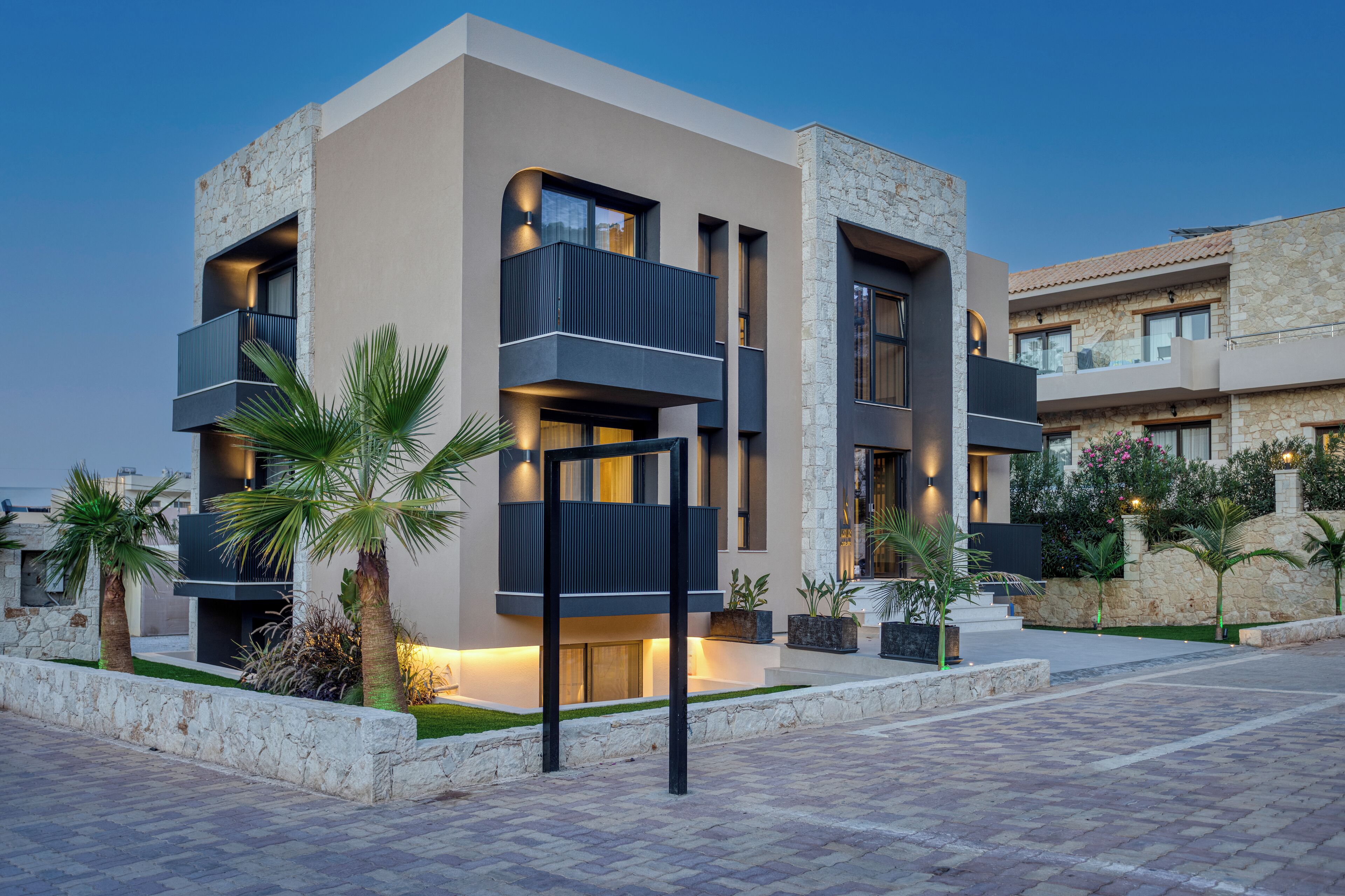 A modern multi-story building with balconies, stone facade, and well-lit outdoor areas.