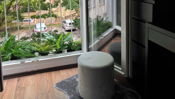 Een moderne kamer met een groot raam, een grijze poef en een ronde tafellamp.