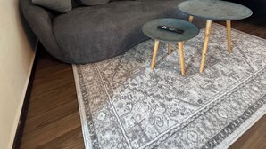 Een moderne woonkamer met een grijze bank, een klein rond tafeltje en een vloerkleed met dessin.