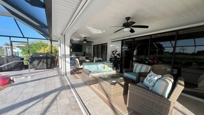 Un patio coperto con mobili in vimini, una ventola a soffitto e vista sul giardino.
