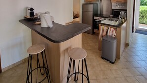A modern kitchen with a central island, two bar stools, stainless steel appliances, and a view of greenery outside.