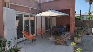 A patio area with a table and chairs, a lounge chair, and potted plants.