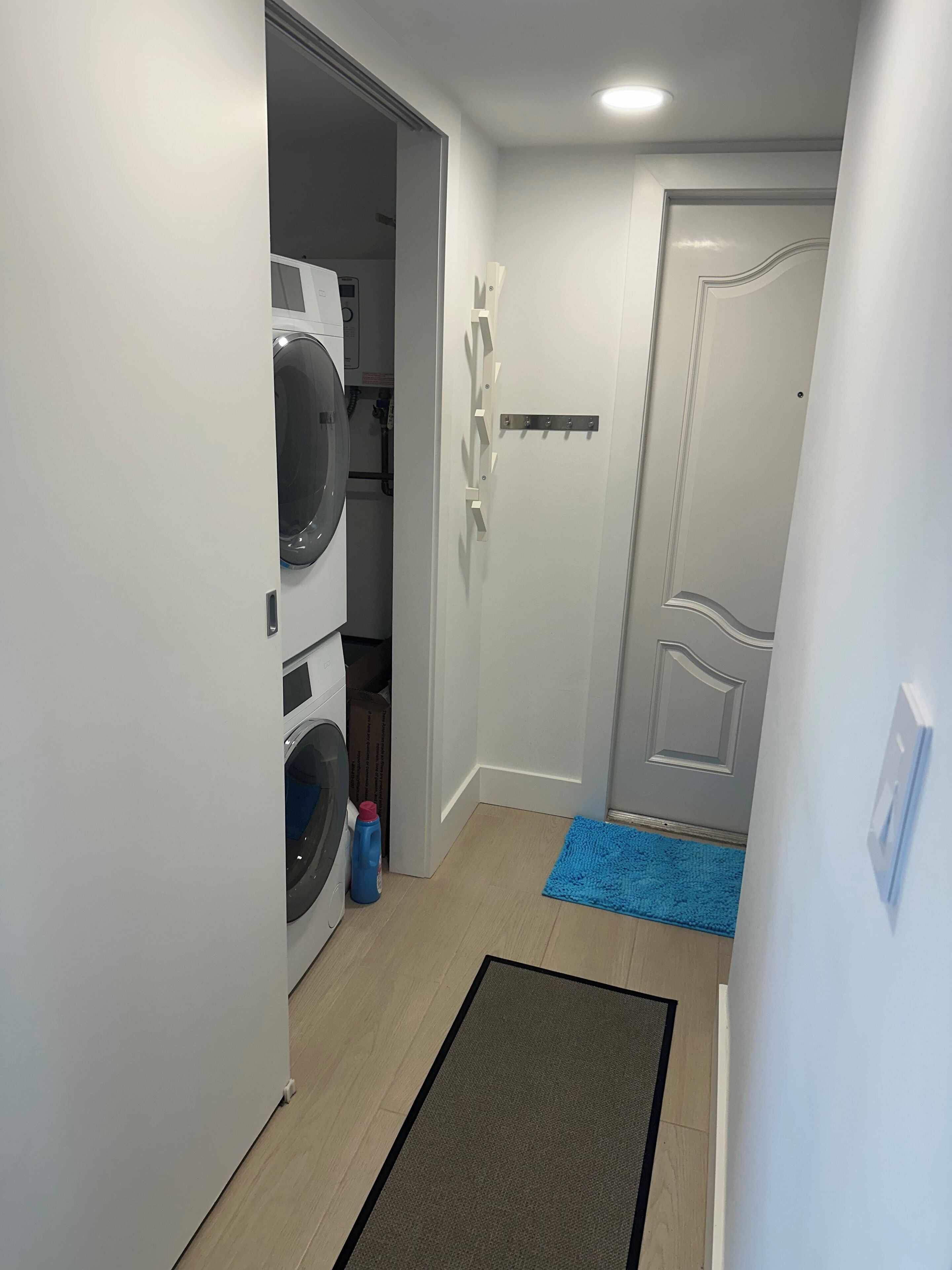A laundry room with stacked washers and dryers, a blue mat, and a door with a handle.