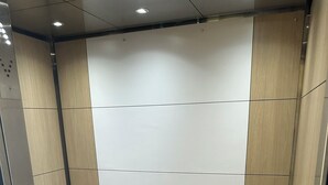 Interior de ascensor con pared de paneles de madera, barandilla de metal y suelo estampado.