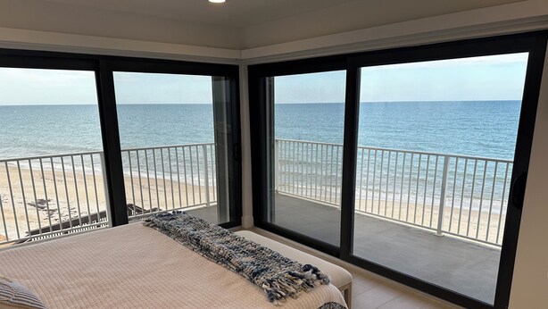 Un dormitorio con una cama grande, vista a la playa y un balcón con barandilla.
