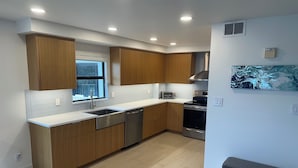 Una cocina moderna con armarios de madera, un lavavajillas de acero inoxidable, un horno empotrado y un ventanal que proporciona luz natural.
