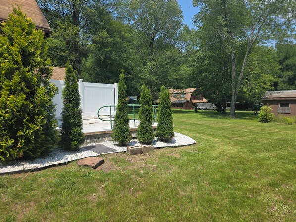 A well-maintained backyard with a white fence, a small deck, and several evergreen trees.