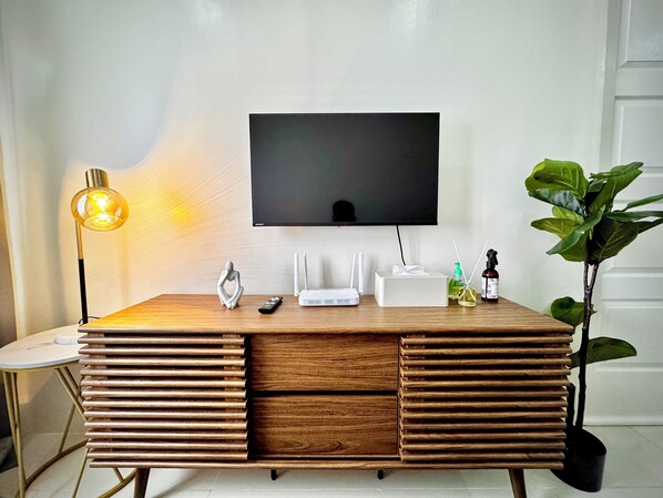 Un salon moderne avec un meuble de rangement en bois pour l’équipement audiovisuel, un téléviseur fixé au mur, une lampe et une plante en pot.