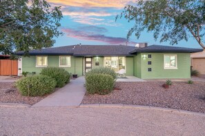 A green single-story house with a front porch, a small patio, and a gravel driveway.