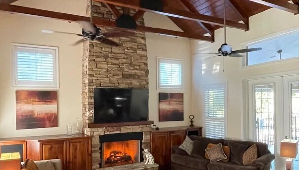 Ein geräumiges Wohnzimmer mit Kamin aus Stein, Holzbalkendecke und großem Fernseher.