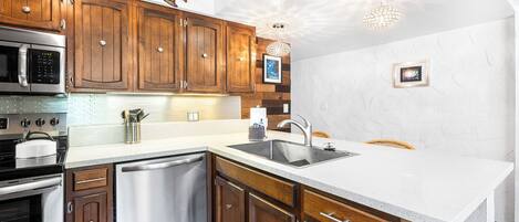 A modern kitchen with wooden cabinets, stainless steel appliances, and a white countertop.
