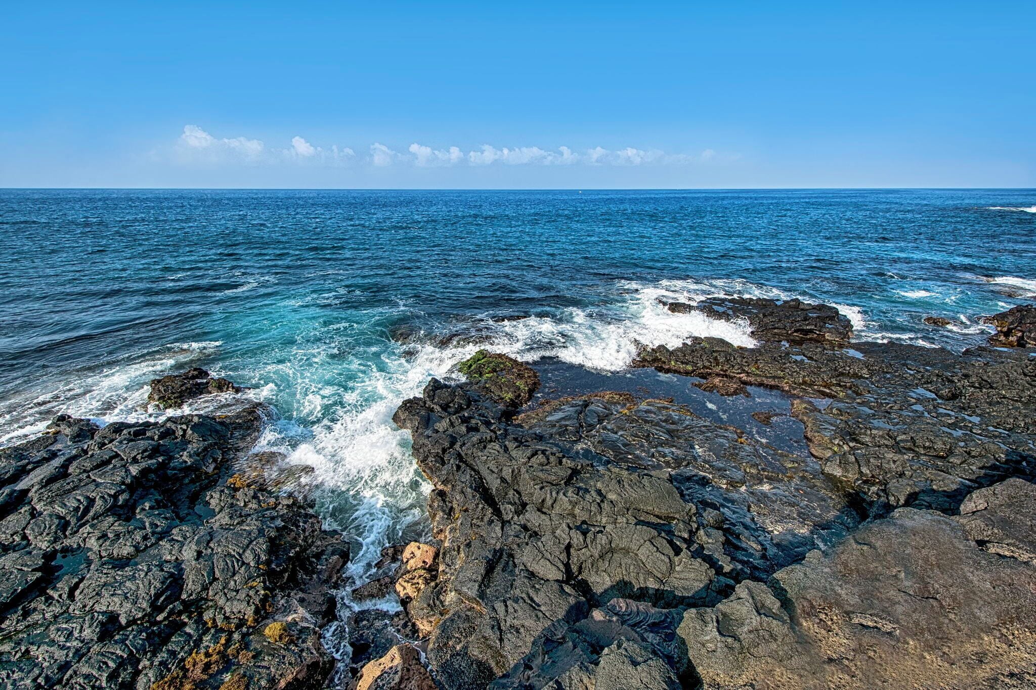 Eine felsige Küste mit brechenden Wellen unter blauem Himmel.