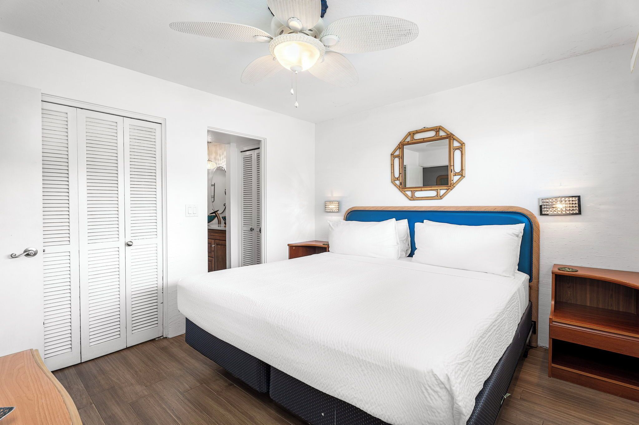 A neatly arranged bedroom with a large bed, a ceiling fan, a wooden headboard, and a mirror on the wall.