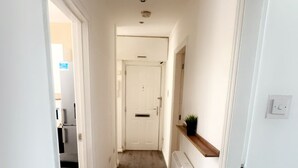 A narrow hallway with wooden flooring, white walls, and a door at the end.