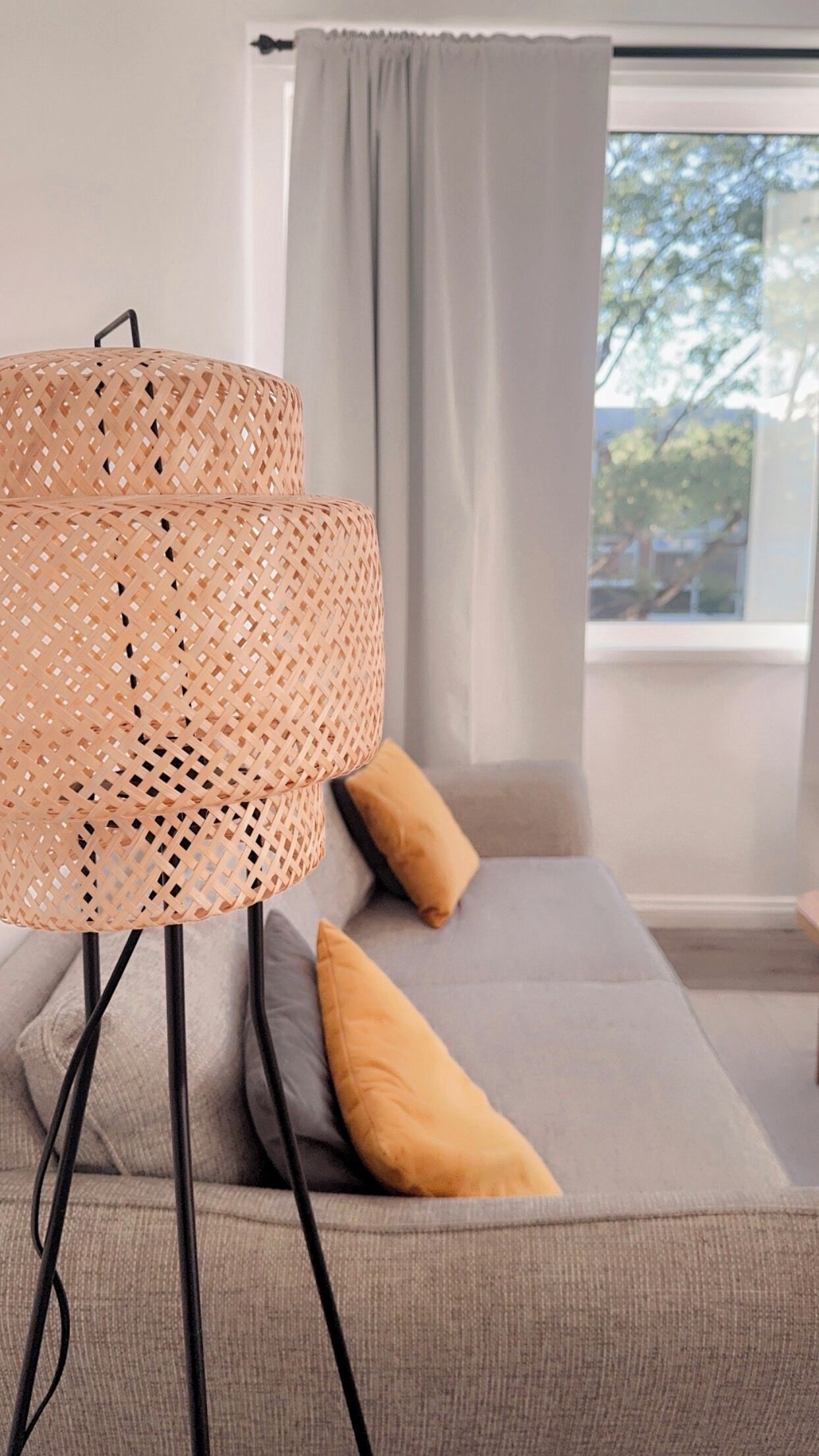A room with a grey sofa, two yellow cushions, and a woven floor lamp.