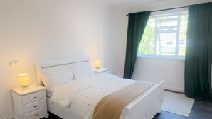 A bedroom with a bed, two bedside tables with lamps, a window with curtains, and a skylight.