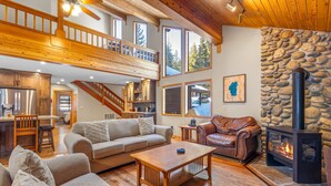 A spacious living area with a wooden ceiling, a stone fireplace, and a view of the outdoors through large windows.