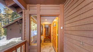 A wooden exterior with a snow-covered deck and a stone-tiled entrance.