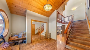 A spacious room with wooden flooring, a staircase, and a large mirror reflecting the interior.