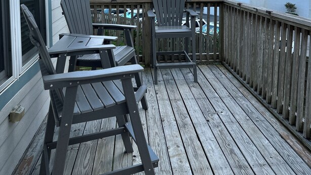 Une terrasse en bois avec deux fauteuils Adirondack et une petite table, donnant sur un parking et un bâtiment blanc doté de balcons.