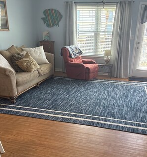 A living room with a sofa, a red armchair, a blue rug, and a fish wall decoration.