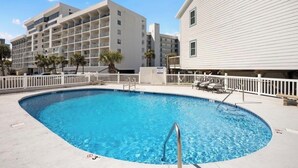 Une piscine dont la profondeur est indiquée à 3 pieds, entourée d’une clôture blanche, avec un immeuble à plusieurs étages en arrière-plan.