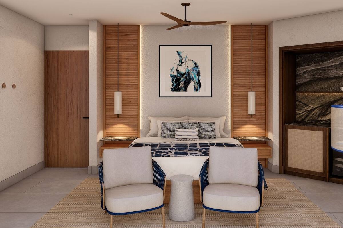 A modern bedroom with a bed, two chairs, a side table, a ceiling fan, and a large artwork on the wall.
