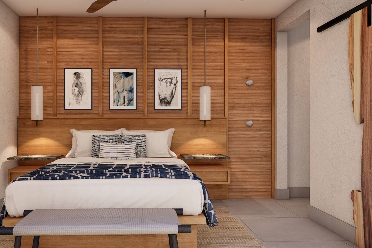 A modern bedroom with a wooden headboard, a large bed with patterned bedding, bedside lamps, and three framed artworks on the wall.