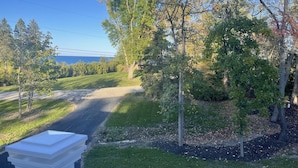A residential driveway with a white column, surrounded by trees and a lawn.