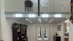 A spacious living area with a high ceiling, a chandelier, a staircase leading to an upper level, and a view of the outdoors through glass doors.