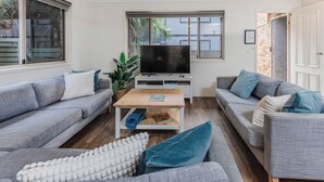 A modern living room with two grey sofas, a wooden coffee table, a flat-screen TV, and a ceiling fan. - High Tide Hideaway in Pottsville (Pottsville)