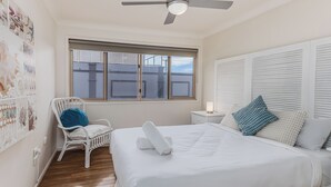 A bedroom with a bed, a chair, a bedside table with a lamp, a ceiling fan, and a window with blinds. - High Tide Hideaway in Pottsville (Pottsville)