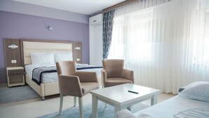 A hotel room with a bed, two armchairs, a small table, a nightstand, and a window with sheer curtains. - EMERALD Hotel (Ulcinj)