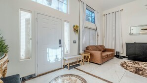 Un salón amplio con un gran ventanal, un sofá marrón, un pequeño banco y una alfombra decorativa.
