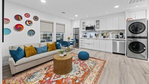 A modern kitchen with stainless steel appliances, a dining area with a blue chair, and a living room with a sofa and colorful pillows. - Moroccan-Inspired 1-BR Getaway near Reunion Tower (Dallas)