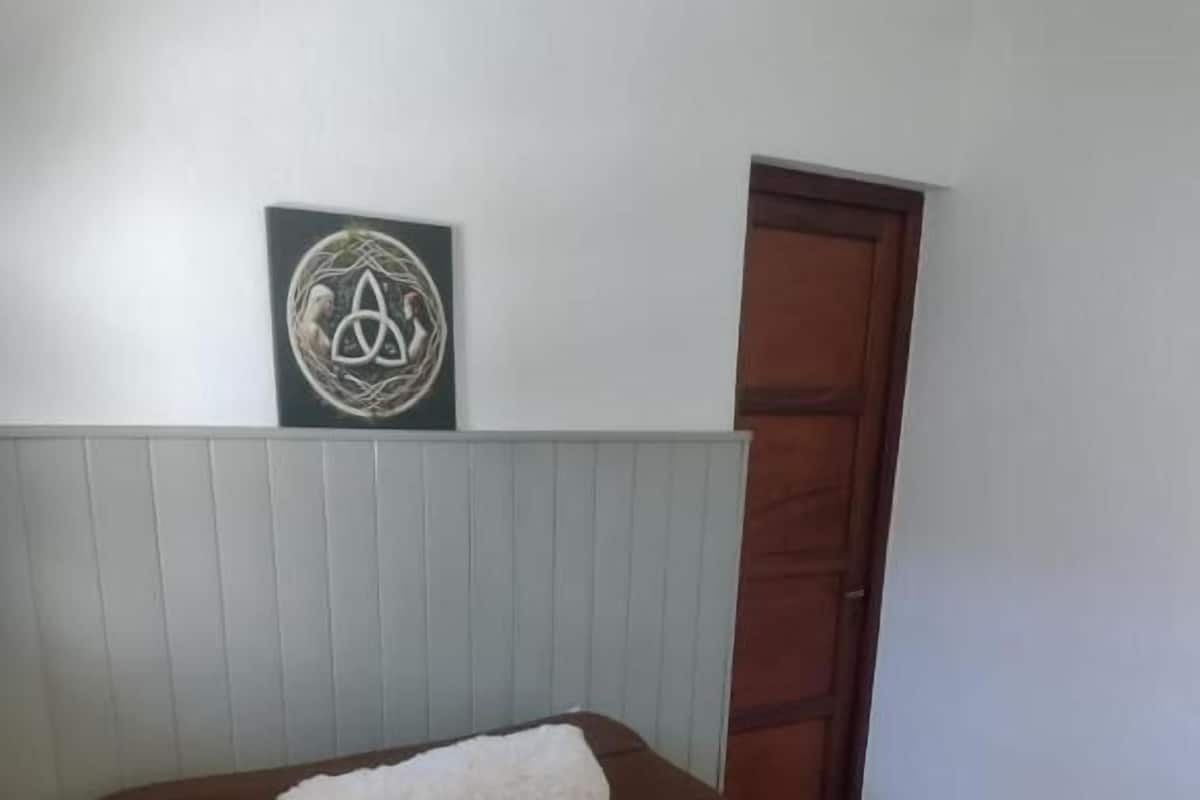Ein ordentlich gemachtes Bett mit einer braunen Bettdecke, einem weißen Kopfkissen, zwei gefalteten weißen Handtüchern und einem gerahmten Kunstwerk darüber.
