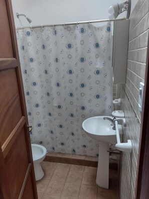 A bathroom with a patterned shower curtain, a white sink, and a toilet. - Hostal Avalon (Capilla del Monte)