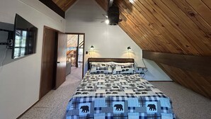 A bedroom with a sloped ceiling, a bed with a checkered bear-patterned bedspread, two wall-mounted lamps, and a ceiling fan. - Out of Office: Cozy A-frame cabin in the pines near trails and adventure! (Munds Park)