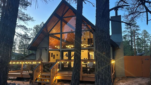A cabin with a large glass facade, wooden deck, and a stone pathway. - Out of Office: Cozy A-frame cabin in the pines near trails and adventure! (Munds Park)