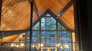 A high-ceilinged room with wooden beams and large windows offering a view of trees. - Out of Office: Cozy A-frame cabin in the pines near trails and adventure! (Munds Park)