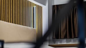 Una habitación de hotel moderna con cama, cabecera de listones de madera y ventana con cortinas.