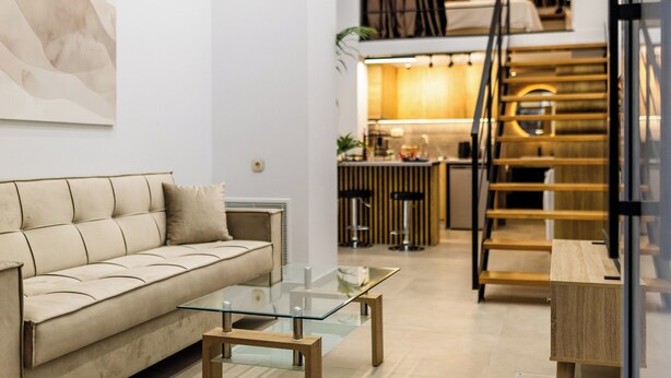 Una sala moderna con un sofá, una mesa de centro de vidrio y una escalera que lleva a una zona de cocina.